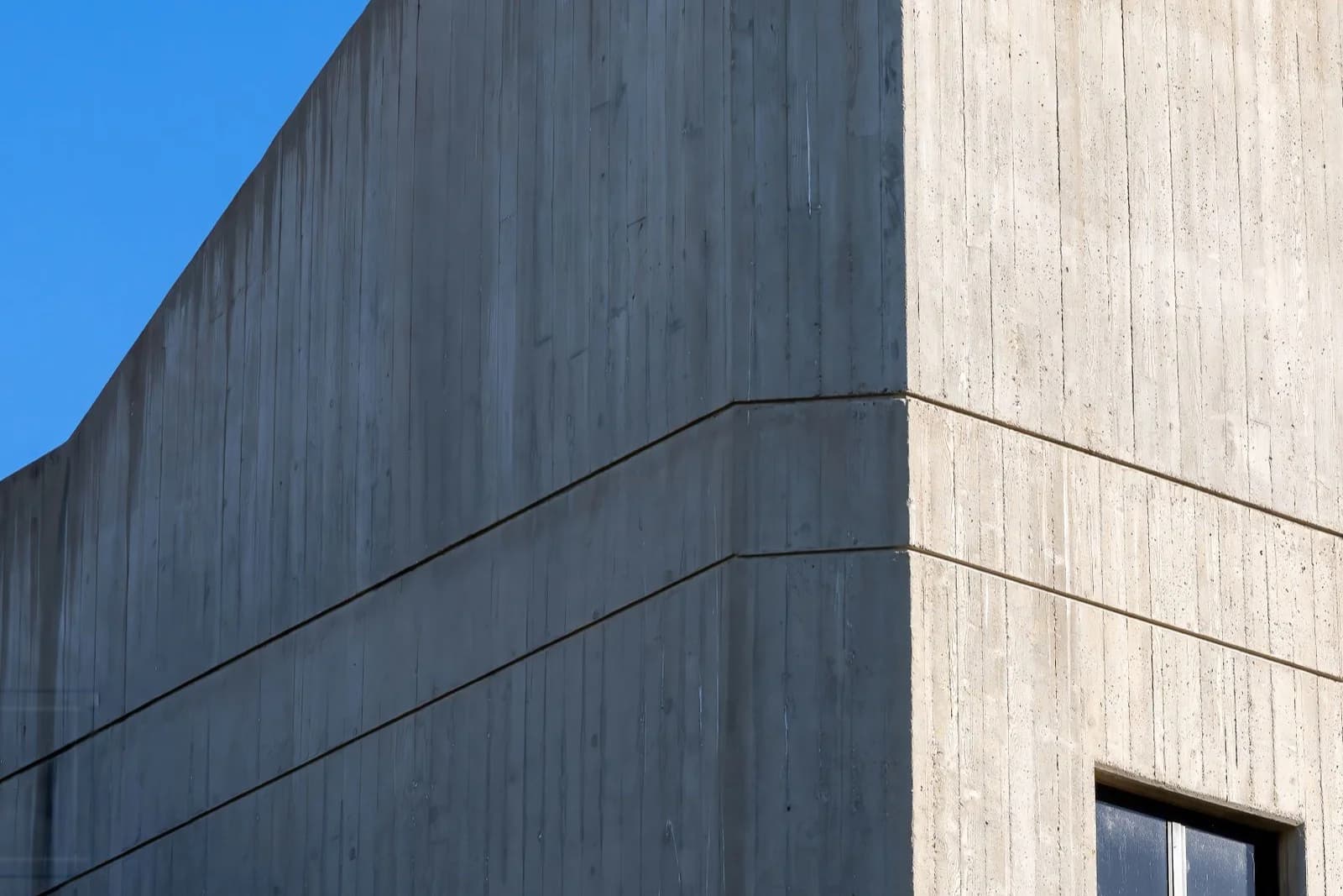 青空を背にした打ちっ放しコンクリート建物の角。質感の異なる二つの壁面が直角に切り替わる外観