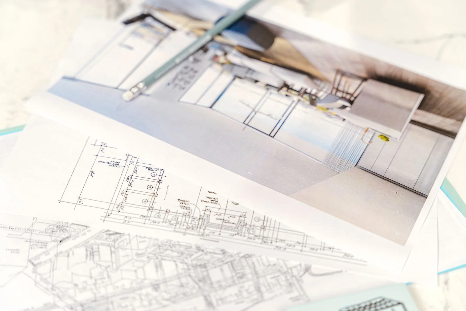 鉛筆を置いた建物の設計図面と内観パースの印刷物が机の上に重ねられている様子